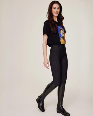 Volledige lichaamsfoto in wandelpose met het zwarte T-shirt met paardenprint en hoogwaardige zwarte rijlegging.