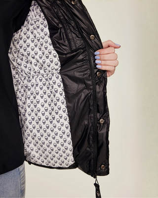 Detailopname van de binnenvoering van de zwarte bodywarmer, uitgevoerd in een unieke witte stof met kleine zwarte schedelprints.