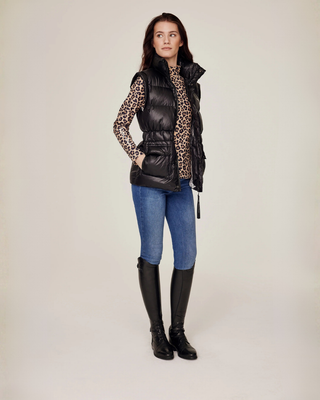 Volledige lichaamsopname vanuit een schuine zijhoek van de open zwarte rijbodywarmer, gestyled met een complete leopard print paardensportoutfit.