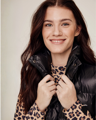 Portret van het model dat de hoge kraag van de zwarte rijbodywarmer vasthoudt, waarbij de premium halfglanzende textuur zichtbaar is.
