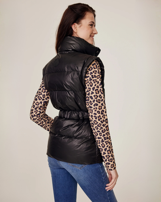 Zijprofielopname van het model dat de halfglanzende zwarte pufferbodywarmer en leopard print rijtop draagt.