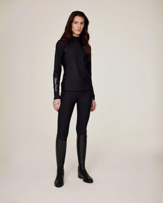 Schuin full-body shot van een model dat de zwarte paardrijtop styled met bijpassende zwarte rijleggings voor een strakke look.