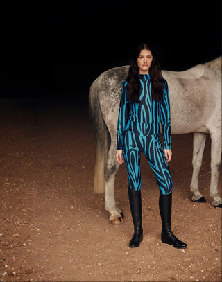 Lifestyle-opname in paardensportstijl van een model in de blauwe zebraset met een grijs paard op de achtergrond.