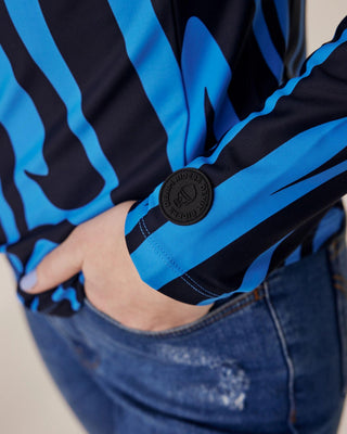 Close-up van de mouw met het Riders Denim-logo op blauwe zebrastof, met de hand van het model in de zak van haar denim rijbroek.