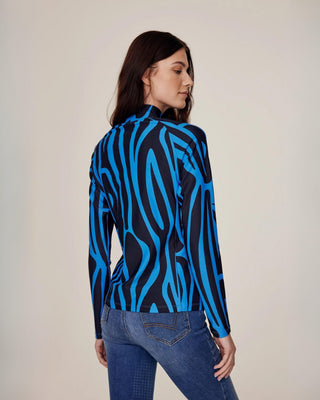 Schuine achteraanzicht van een model dat de blauwe zebra-rijtop met hoge kraag draagt, gecombineerd met originele denim rijbroek.
