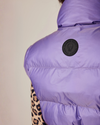 Gedetailleerde close-up van het Riders Denim-logo op de achterkant van het lila puffer vest.