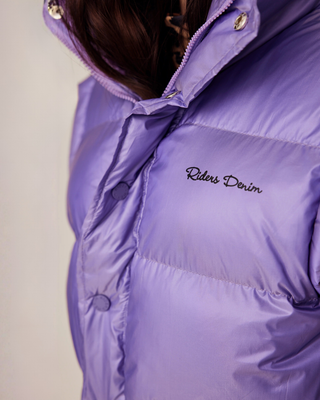 Close-up van de voorkant van het lila vest met de kenmerkende Riders Denim-branding en ritssluiting.