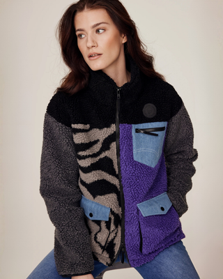 Zittend model poseert met één arm achter haar rug en toont het dichtgeritste lila en zebra rijjack.