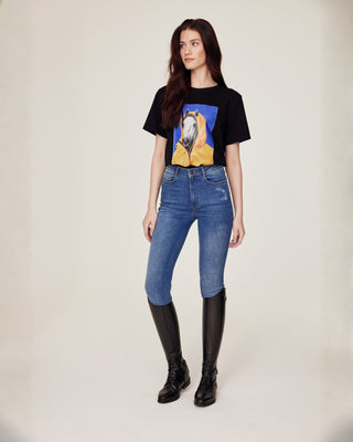 Volledig lichaamsbeeld van voren van een model dat Riders Denim original jeans rijbroek en een zwart t-shirt met paardenprint draagt.