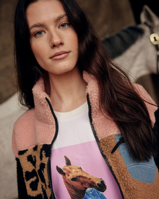 Portret van een model in de Pink and Leo teddyjas en wit t-shirt met paardenprint met een grijs paard op de achtergrond.