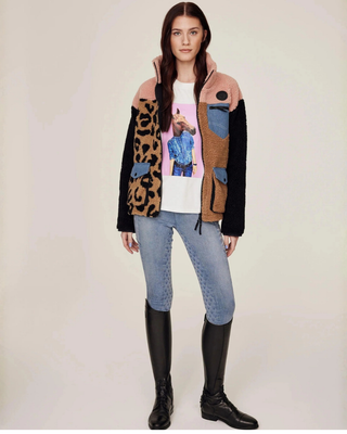 Volledig lichaamsaanzicht van de open teddyjas, waarbij het witte t-shirt met paardenprint en de lichtblauwe jeans rijbroek eronder zichtbaar zijn.