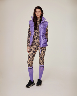 Full-body vooraanzicht van een model in een leo rijset en lila puffer bodywarmer, gestyled met bijpassende lila paardrijsokken.