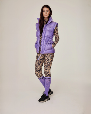Full-body shot van een model in een complete rijset met luipaardprint, lila puffer bodywarmer en bijpassende lila rijsokken.