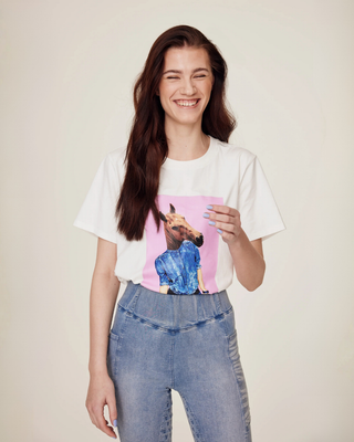 Lachend model dat het witte T-shirt met horsie-print draagt, gecombineerd met lichtblauwe denim rijtights.