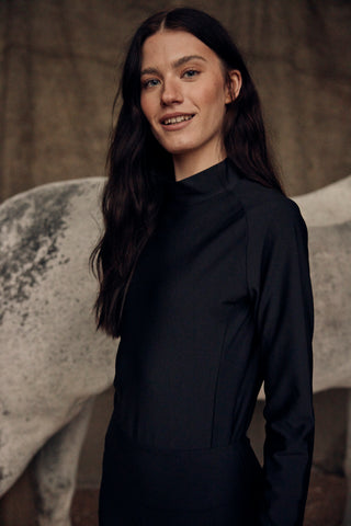 Ruiterportret van een model dat de zwarte paardrijtop met hoge kraag draagt met een grijs paard op de achtergrond.